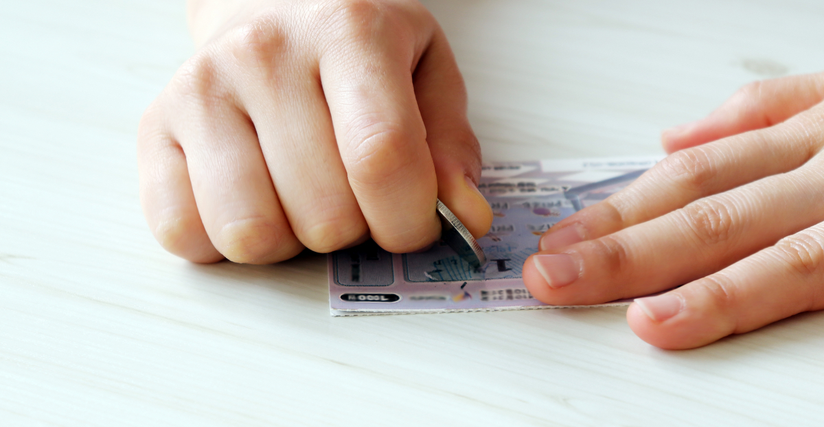 Someone using a coin to play a scratch-off lottery ticket