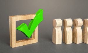 a set of wooden people in line to vote near a green checked box